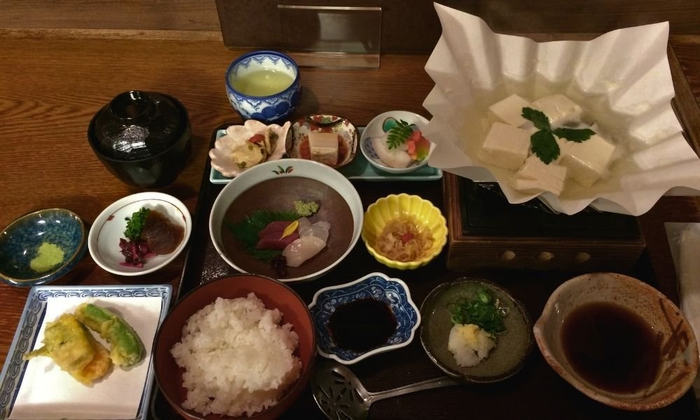 Traditional Kyoto dining experience featuring a beautifully presented kaiseki meal with seasonal dishes, tofu, and matcha tea in an authentic Japanese restaurant setting.