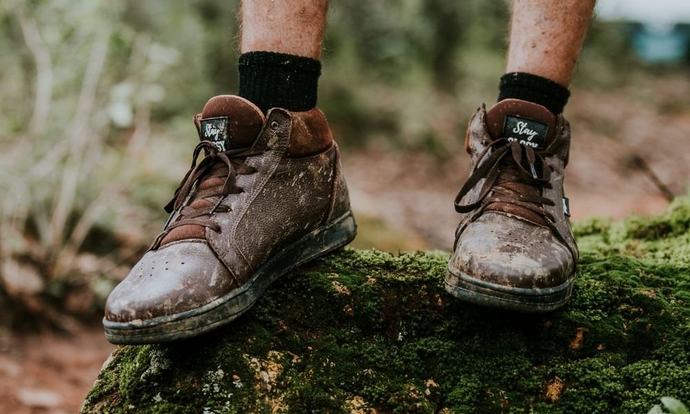 Two pairs of travel shoes on a Norwegian trail showing waterproof hiking boots with mud on the soles beside clean minimal walking shoes for Scandinavia city days