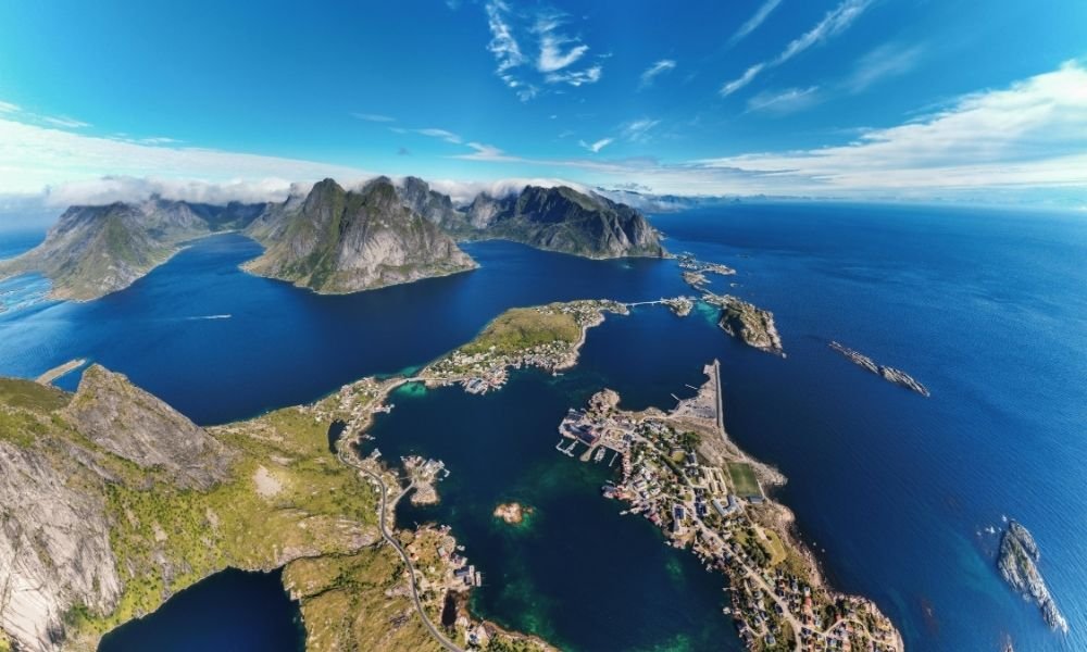 Aerial view of the Stockholm archipelago in summer showing dozens of small pine-covered rocky islands scattered across calm blue water with a white passenger ferry creating a gentle wake