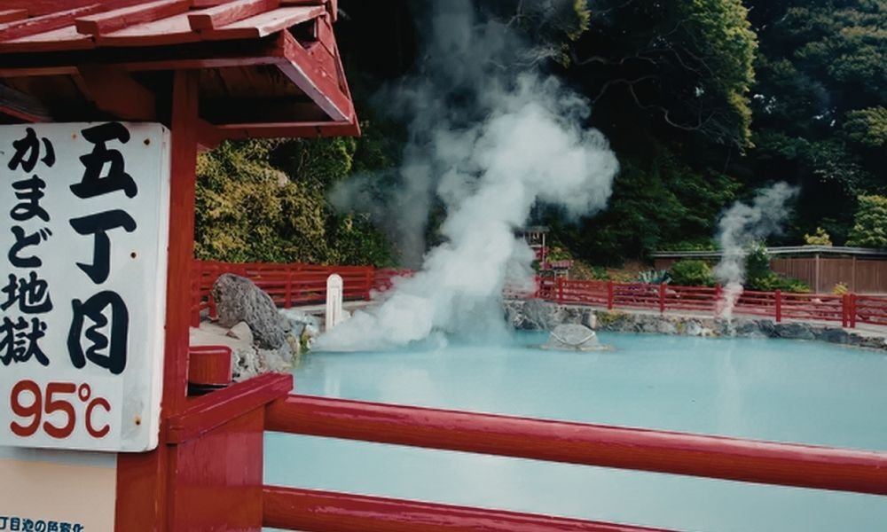 Outdoor hot spring bath at Kurama Onsen in Kyoto, steam rising against cedar forest, mountains in background, wooden fence visible, no people in frame