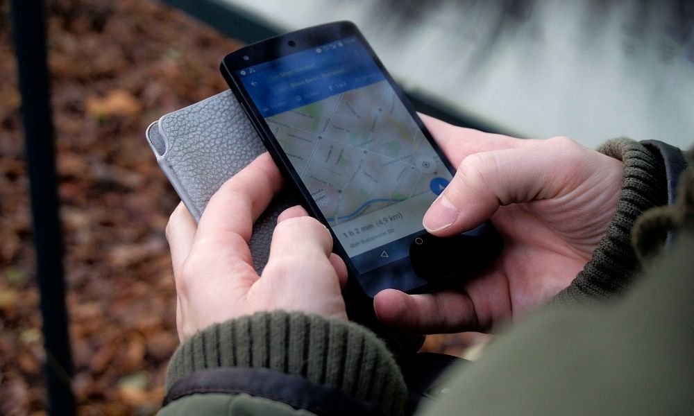 Smartphone screen showing Google Maps with Kyoto subway lines, held in hand with convenience store onigiri wrapper visible`
