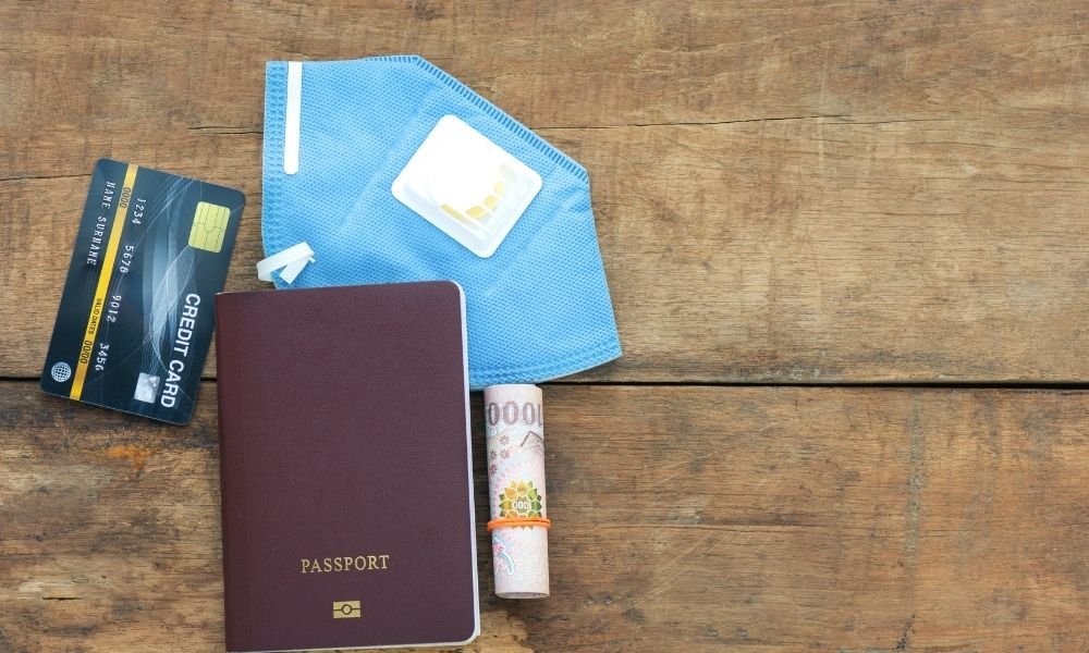 Open ziplock travel pouch with passport copy, cash in tampon wrapper, debit card, and SafetyWing insurance card on wooden table