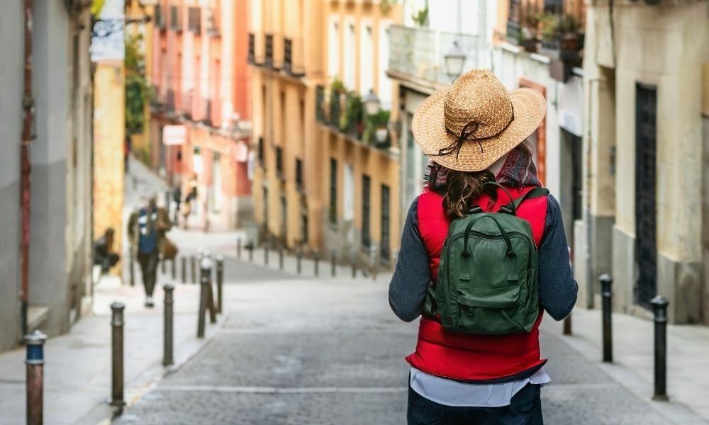 A confident solo female traveler walking through a historic city street while wearing a secure travel backpack.