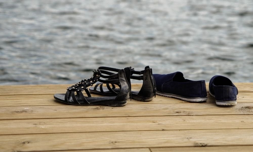 A pair of broken-in walking shoes placed next to a pair of lightweight travel sandals on a neutral background