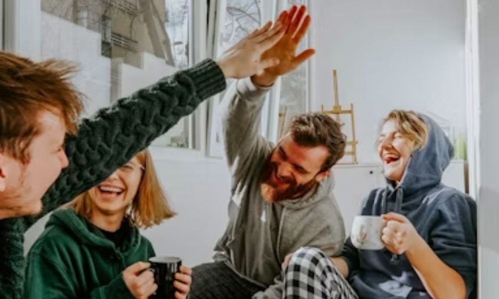 A diverse group of global travellers laughing together at a communal table, showcasing how to make friends while travelling alone.
