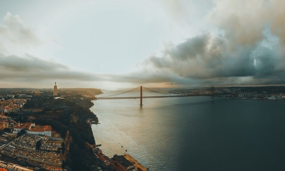 Lisbon skyline at sunset viewed from a miradouro viewpoint with Tagus river and 25 de Abril Bridge