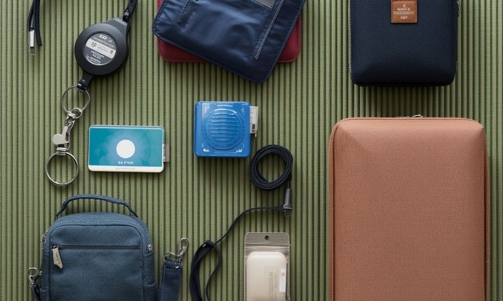 Flat lay of solo travel gear for Japan: IC card on retractable reel, pocket WiFi device, packing cubes in two colors, neck wallet, all on tatami mat