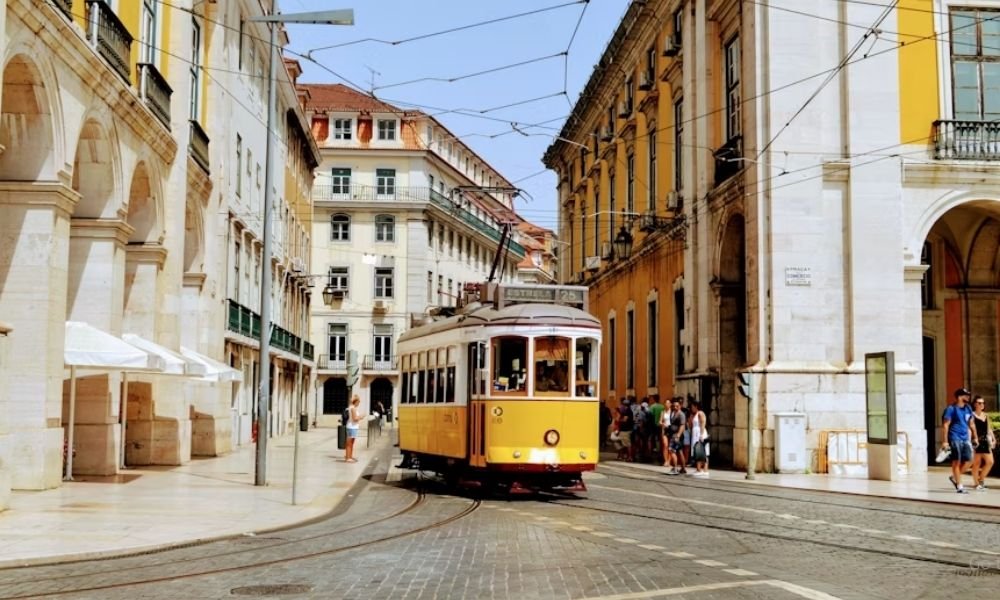 A vibrant yellow tram navigating a scenic, historic street in Lisbon, Portugal, a top destination for first-time solo travel.