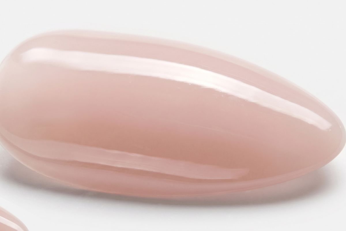 A close-up photograph of an oval, natural-nude false fingernail on a light surface against a grey background.